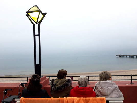 Drei ältere Menschen sitzen auf einer Bank und blicken auf die Ostsee